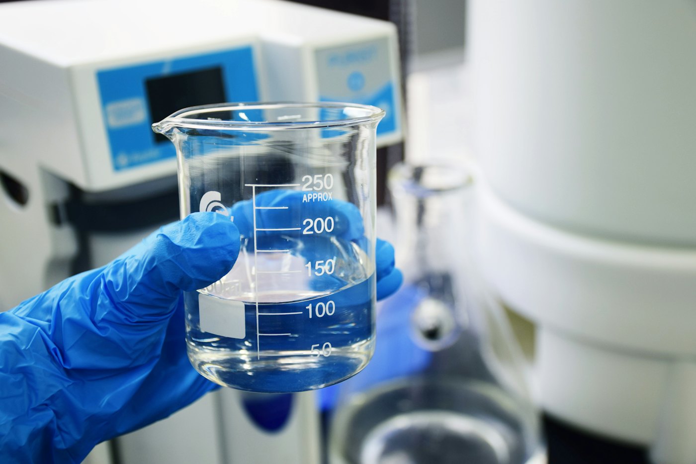 Mão de luva segurando um béquer com água em um laboratório